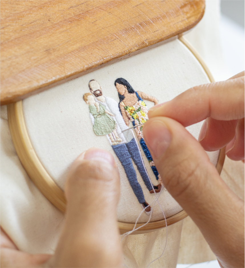 Mãos bordando uma fotografia de família em um bastidor.